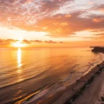 Imagem de um nascer do sol tranquilo sobre o oceano, com luz dourada e atmosfera pacífica.
