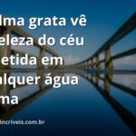Céu azul com nuvens brancas refletido perfeitamente na superfície calma de um lago, cercado por natureza verdejante, transmitindo paz e gratidão.